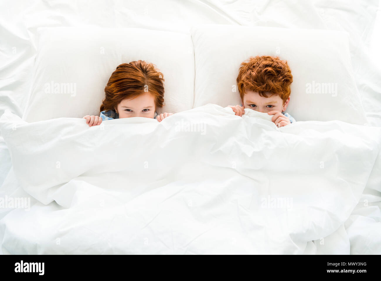 Blick von oben auf die kleine süße rothaarige Kinder versteckt unter Decke im Bett Stockfoto