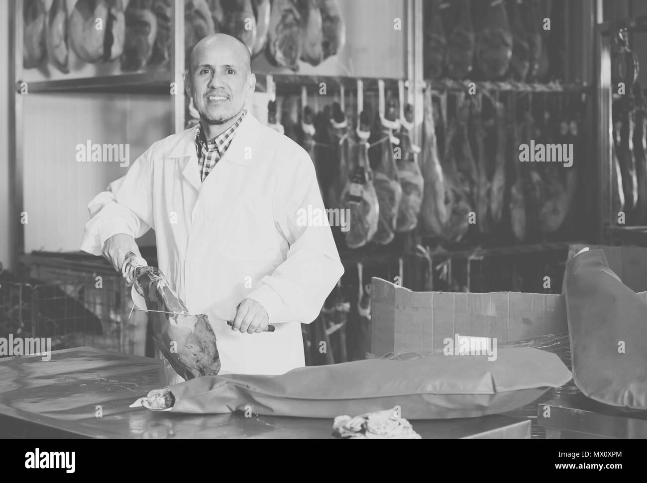 Lächelnd reife Metzger im weißen Overall slicing Jamon im Feinkostgeschäft Stockfoto