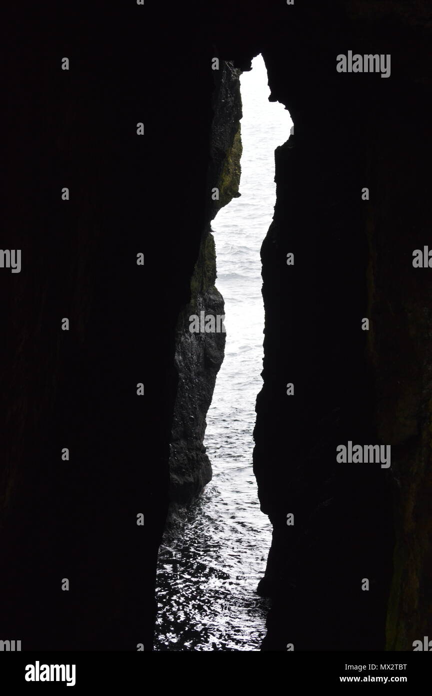 Eine Lücke in einer Höhle am Rande des Meeres lassen Licht in den dunklen Bereich. Stockfoto