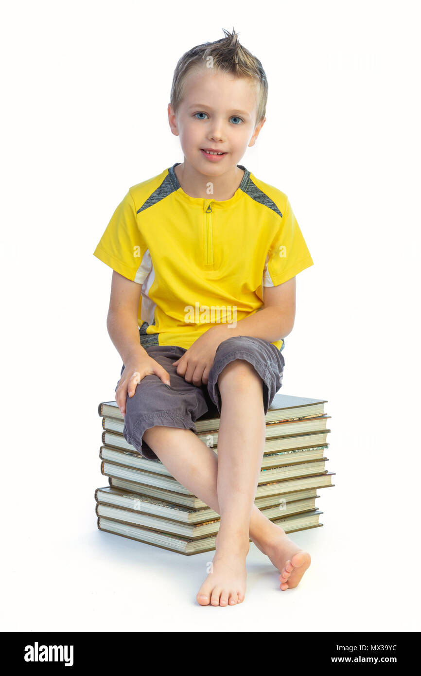 Kind mit einem gelben T-Shirt sitzt auf einem Haufen von Buch auf weißem Hintergrund Stockfoto