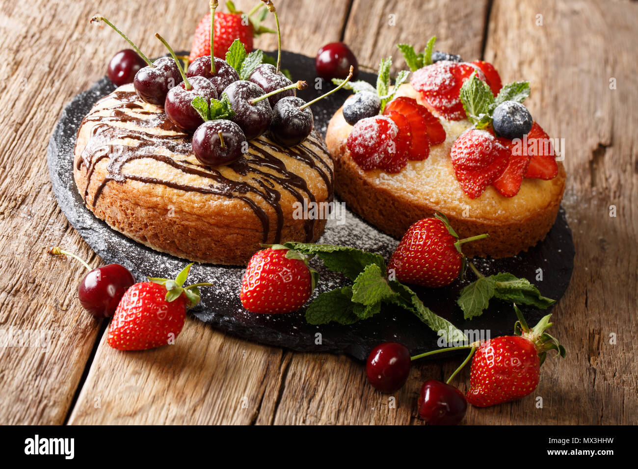 Natürliche organische Kuchen mit Schokolade, Puderzucker, Minze, Erdbeeren, Kirschen und Heidelbeeren in der Nähe eingerichtet - bis auf einer Schiefertafel board. Horizontale Stockfoto