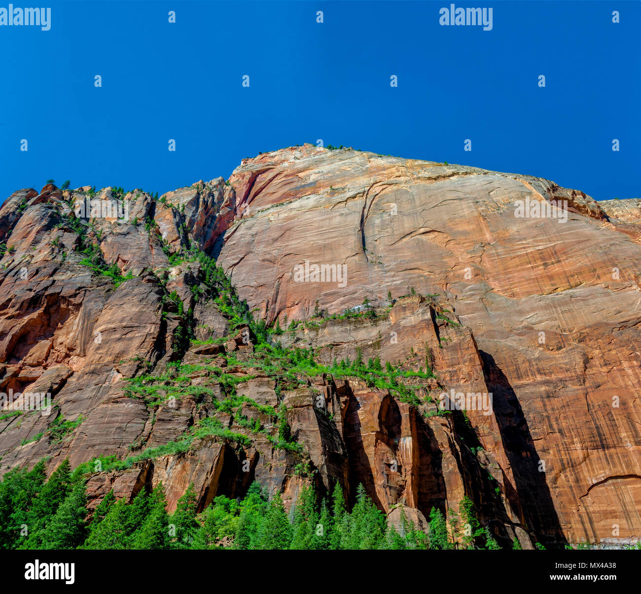 Hohe Solid Rock Mountain mit grüner Vegetation wächst unter strahlend blauem Himmel. Stockfoto