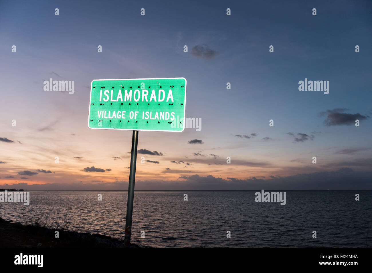 Sonnenaufgang in Islamorada, Florida Keys, mit orange Blauer Himmel, Strand, grünes Schild closeup, Dorf der Inseln im Atlantischen Ozean, Golf von Mexiko, Horizon Stockfoto