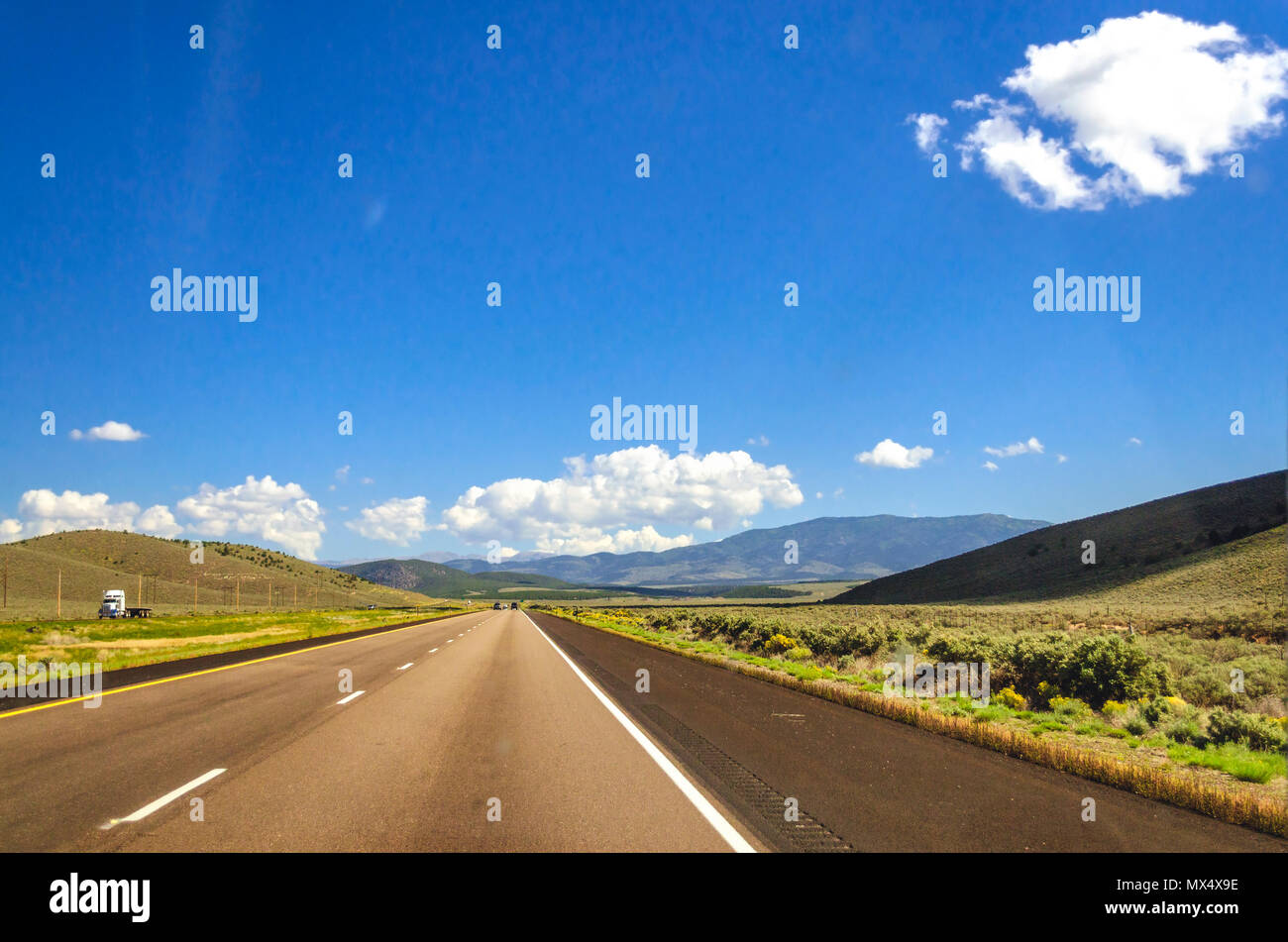 Freeway in der Landschaft mit sanften Hügeln und Feldern unter einem blauen Himmel mit weißen flauschigen Wolken. Stockfoto