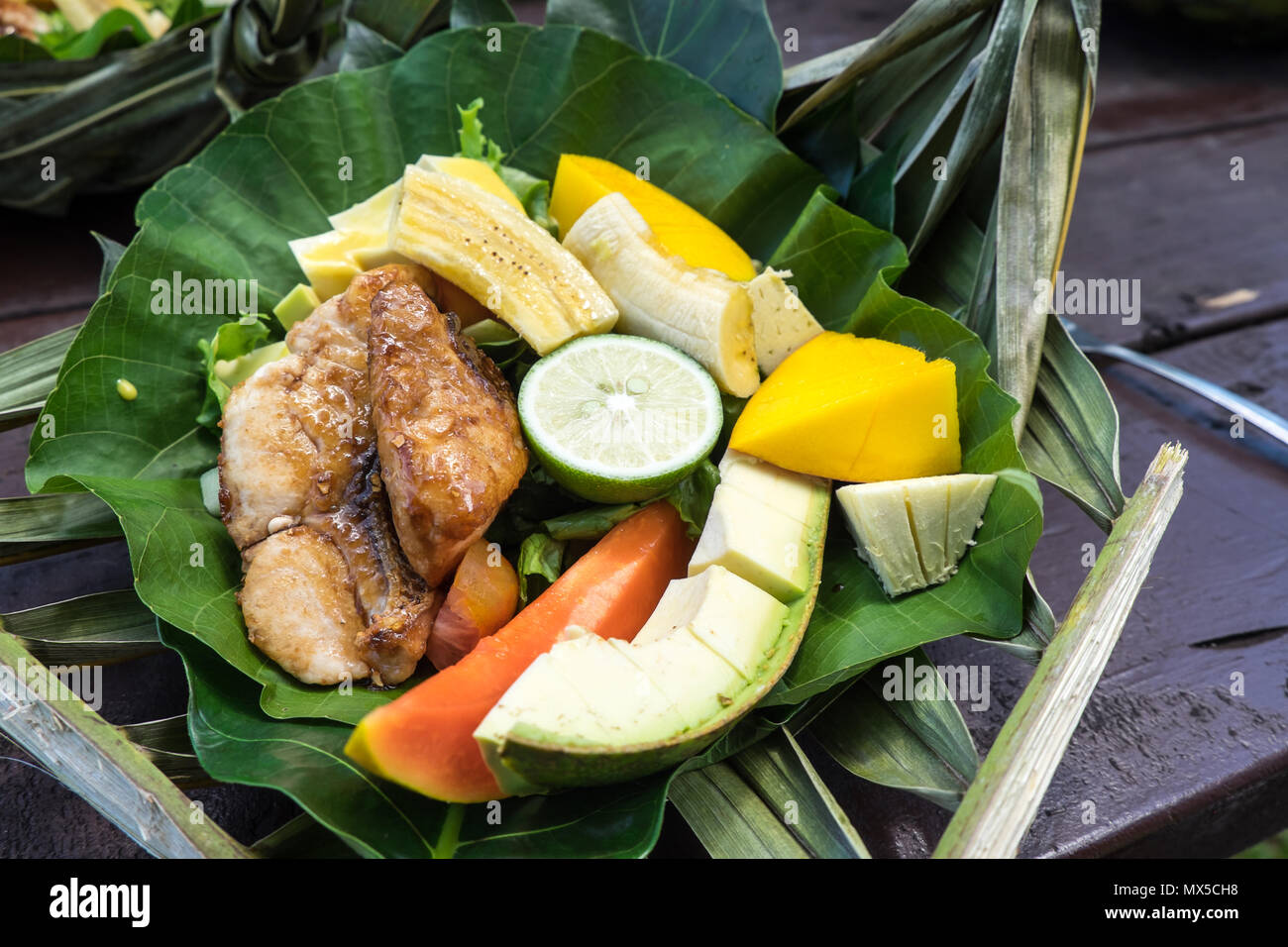 Gesundes Mittagessen mit Fisch und Salat von frischem Obst und Gemüse auf einem biologisch abbaubaren leaf Platte: Banane, Kalk, Brotfrucht, Papaya, Mango-fotografiert Stockfoto