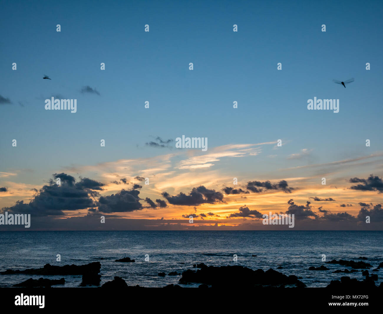 Dramatische bunten Sonnenuntergang über dem Pazifischen Ozean, Hanga Roa, Rapa Nui, Chile mit Felsen im Vordergrund Stockfoto