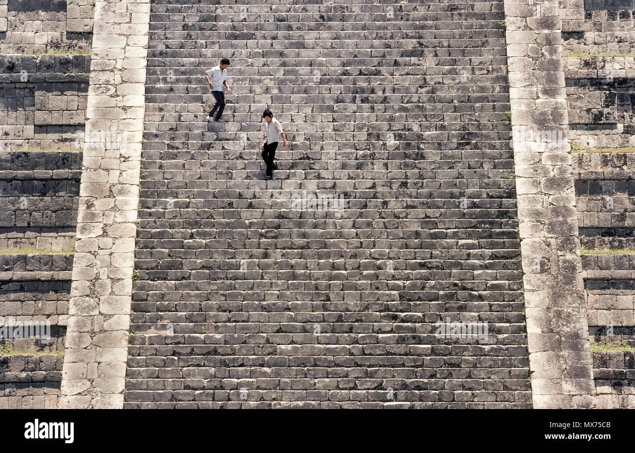 Zwei junge Männer im Zickzack steil nach unten 91 Kalkstein Schritte nach dem Aufstieg auf den Gipfel des El Castillo (das Schloss), auch als der Tempel des Kukulcan, der berühmteste Maya in den antiken Ausgrabungsstätten von Chichen Itza auf der Halbinsel Yucatan in Mexiko Ruine bekannt. Die schmalen Treppen waren in einem Winkel von 45 Grad auf allen vier Seiten dieses pyramidenförmige Struktur aufgebaut. Seit ein Bergsteiger bis zu ihrem Tod im Jahr 2006 fiel, Besucher sind nicht mehr erlaubt, die 99 Fuß - hohe (30-meter) Denkmal, das im 12. Jahrhundert gebaut wurde, um aufzusteigen. Diese präkolumbianischen Sehenswürdigkeit ist ein UNESCO-Weltkulturerbe. Stockfoto