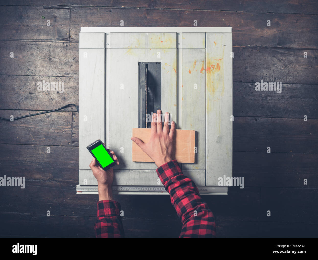 Ein junger Mann einen tablesaw hält eine Chroma Key smart phone und wird von der Gefahr abgelenkt Stockfoto