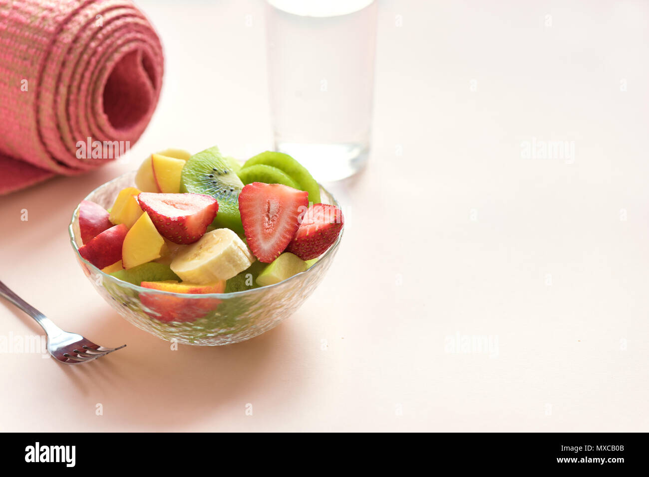 Sport und eine gesunde Lebensweise. Rosa Yoga Matte und Obst und Beeren Salat in der Schüssel für Snack oder Frühstück auf Rosa pastell Hintergrund, kopieren. Stockfoto