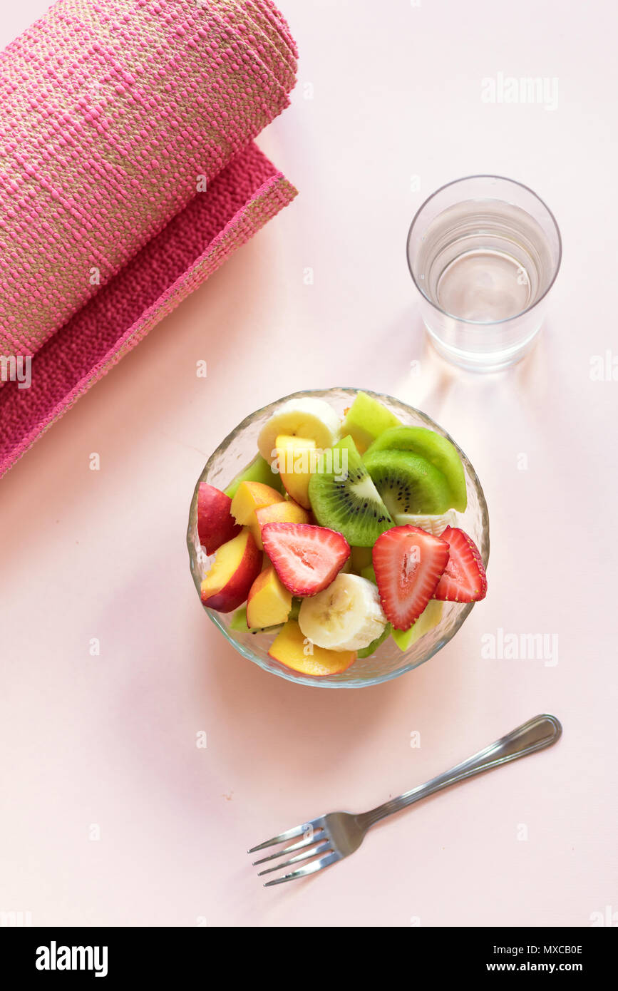 Sport und eine gesunde Lebensweise. Rosa Yoga Matte und Obst und Beeren Salat in der Schüssel für Snack oder Frühstück auf Rosa pastell Hintergrund, kopieren. Stockfoto