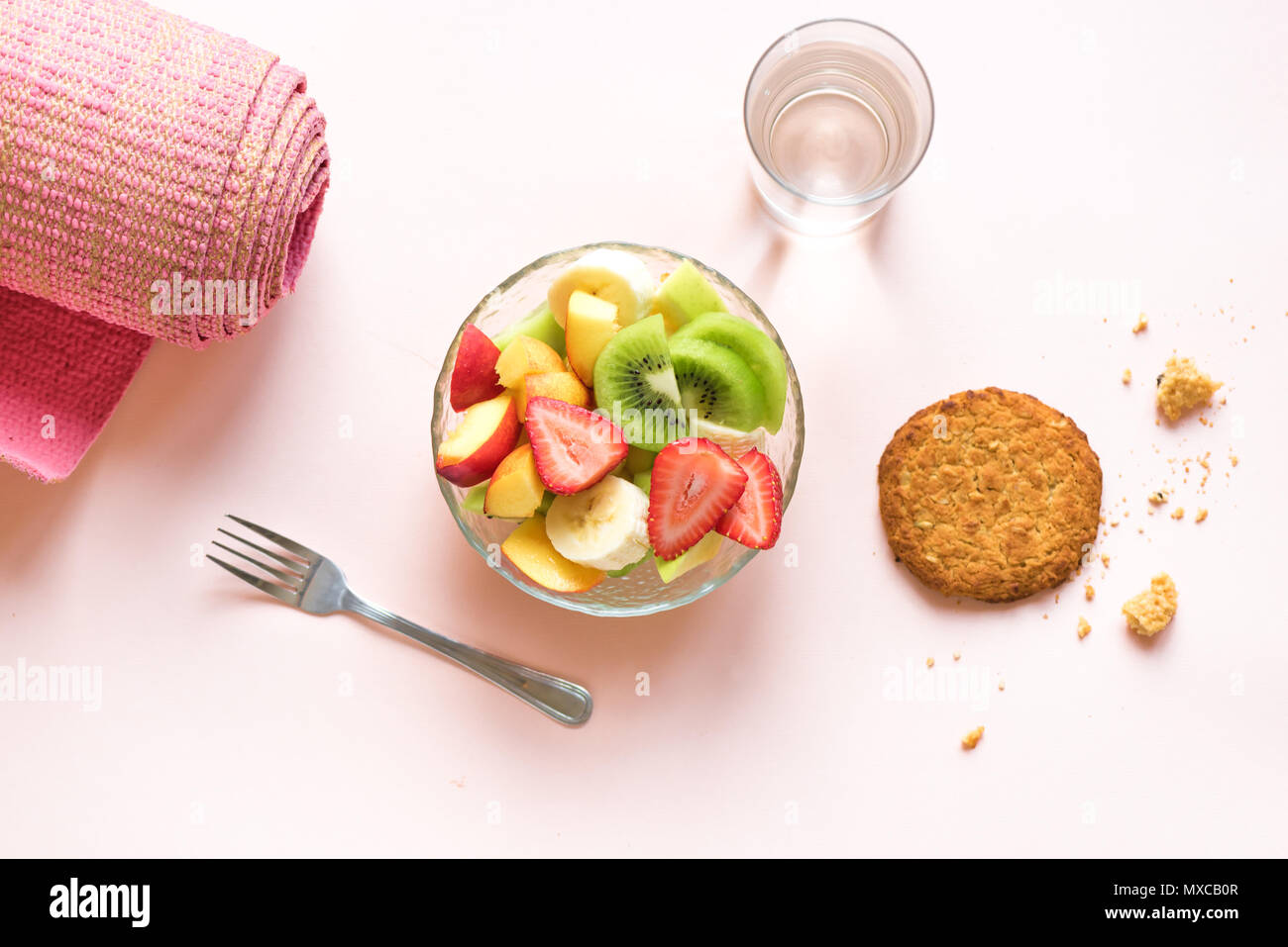 Sport und eine gesunde Lebensweise. Rosa Yoga Matte und Obst und Beeren Salat in der Schüssel und Vollkorn Cookie für Snack oder Frühstück auf Rosa pastell Bac Stockfoto