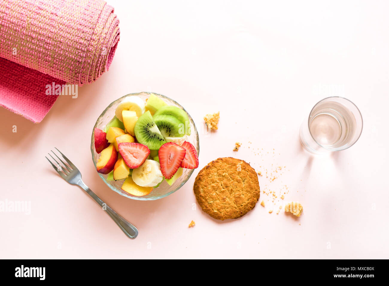 Sport und eine gesunde Lebensweise. Rosa Yoga Matte und Obst und Beeren Salat in der Schüssel und Vollkorn Cookie für Snack oder Frühstück auf Rosa pastell Bac Stockfoto