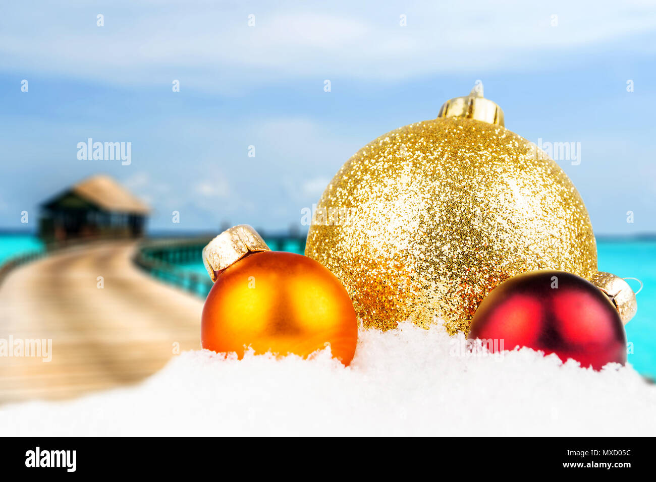 Thema Weihnachten mit Malediven unscharfen Hintergrund, Holz- Bungalows im Hintergrund und Drei bunte Weihnachtskugeln in der Front Stockfoto