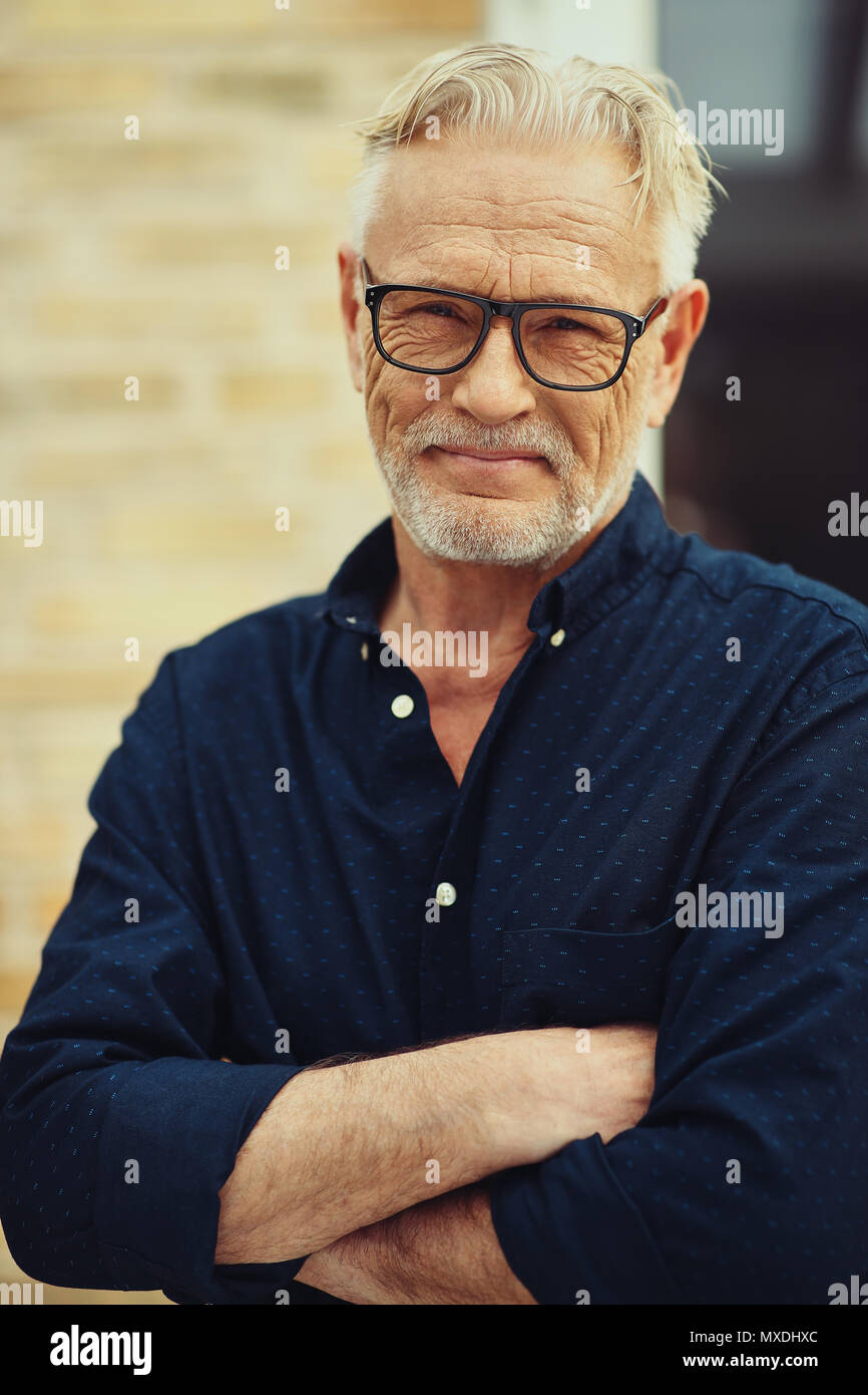 Lächelnd älterer Mann mit Bart und Brille trägt mit seinen Armen außerhalb in seinem Hof zu Hause gekreuzt Stockfoto