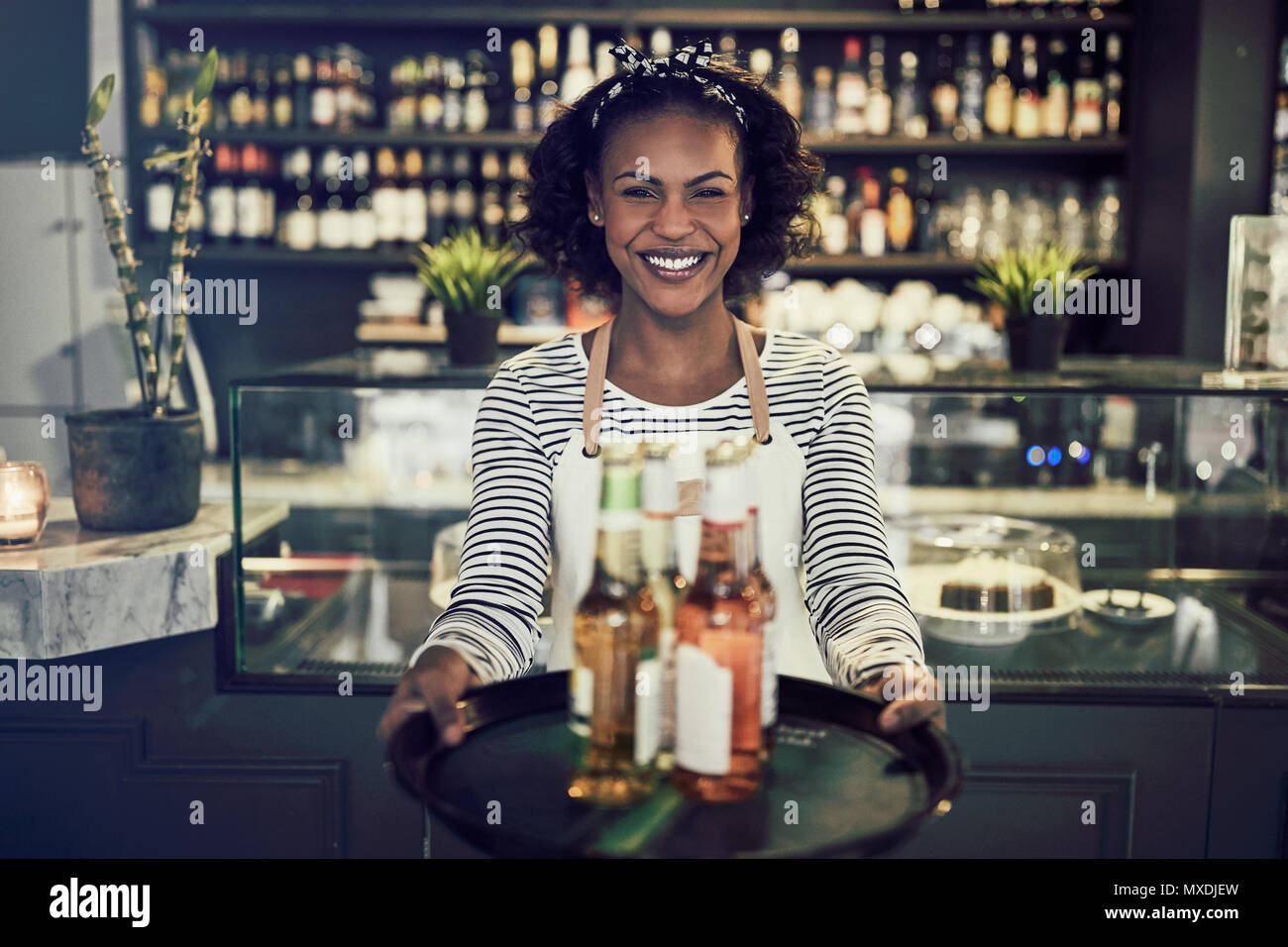 Lächelnden jungen afrikanischen Kellnerin in einem trendigen Restaurant Holding ein Tablett mit bunten Getränke Stockfoto