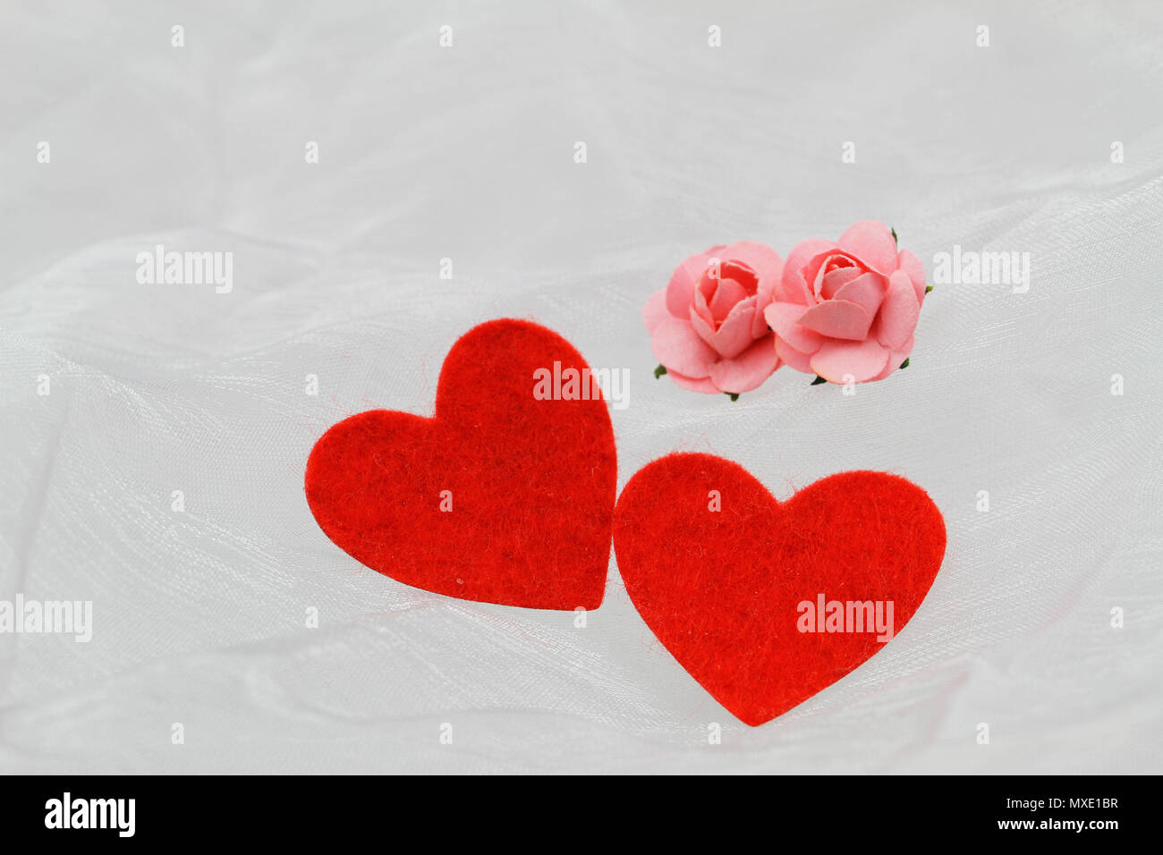 Zwei rote Herzen und zwei Rosa wenig Papier Rosen auf Weiß Textil mit Platz kopieren Stockfoto