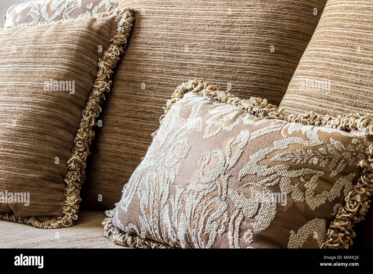 Eine elegante braune bestickte Kissen rund um normale Kissen mit Garn  Bordüren, die alle über eine Couch Stockfotografie - Alamy