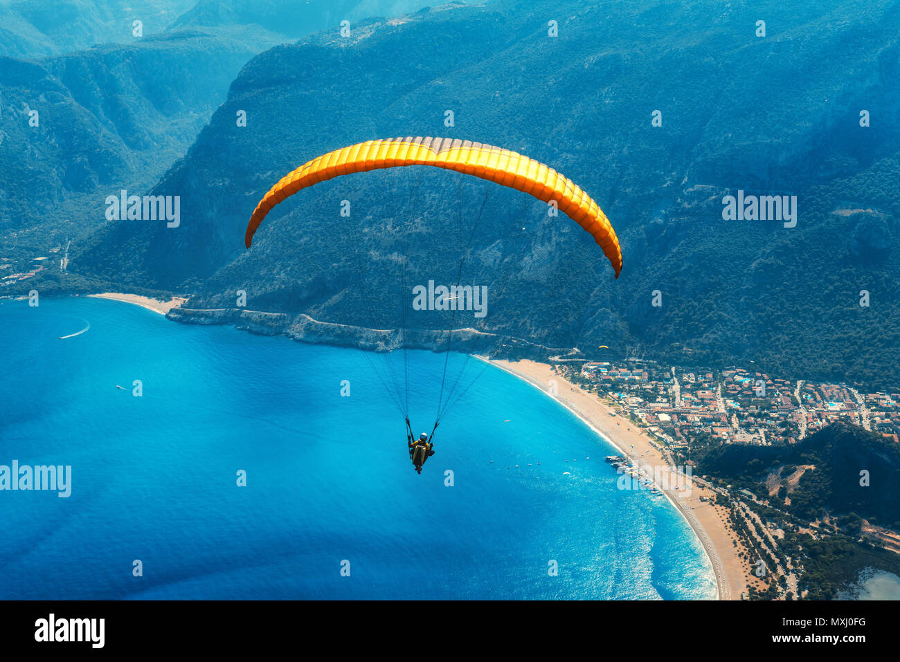 Gleitschirmfliegen in den Himmel. Gleitschirm Tandem über das Meer mit blauem Wasser, Strand und Berge im Sunrise fliegen. Luftaufnahme von Gleitschirm und blauen Lago Stockfoto