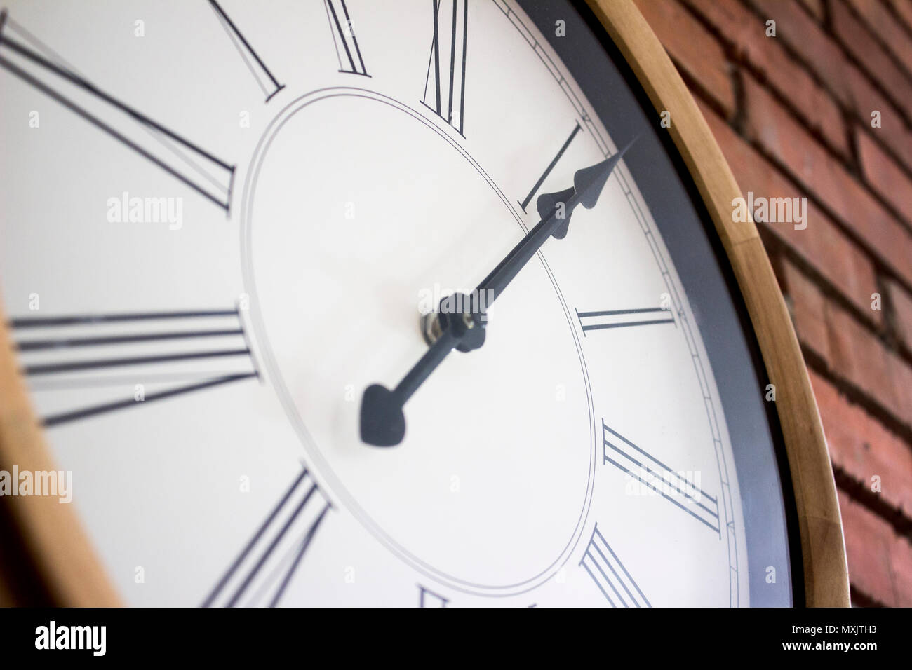 Seite Close-up eine hölzerne Wanduhr mit römischen Ziffern in einem roten Backsteingebäude an der Wand hängen. Stockfoto