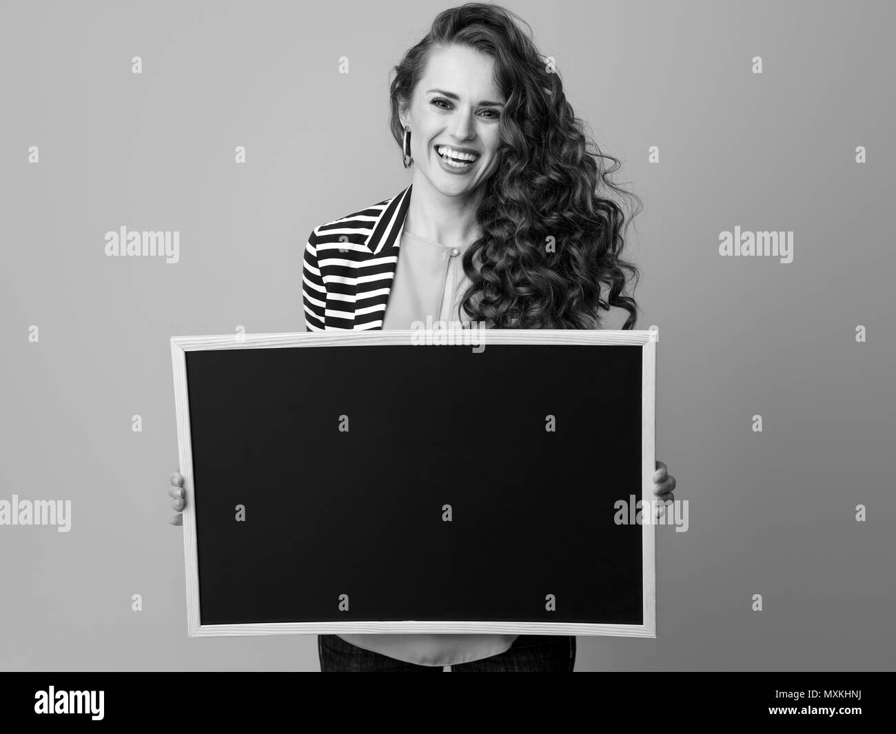 Lächelnd stilvolle Frau mit langen Welligen brünette Haar gegen Hintergrund anzeigen Blank Board Stockfoto