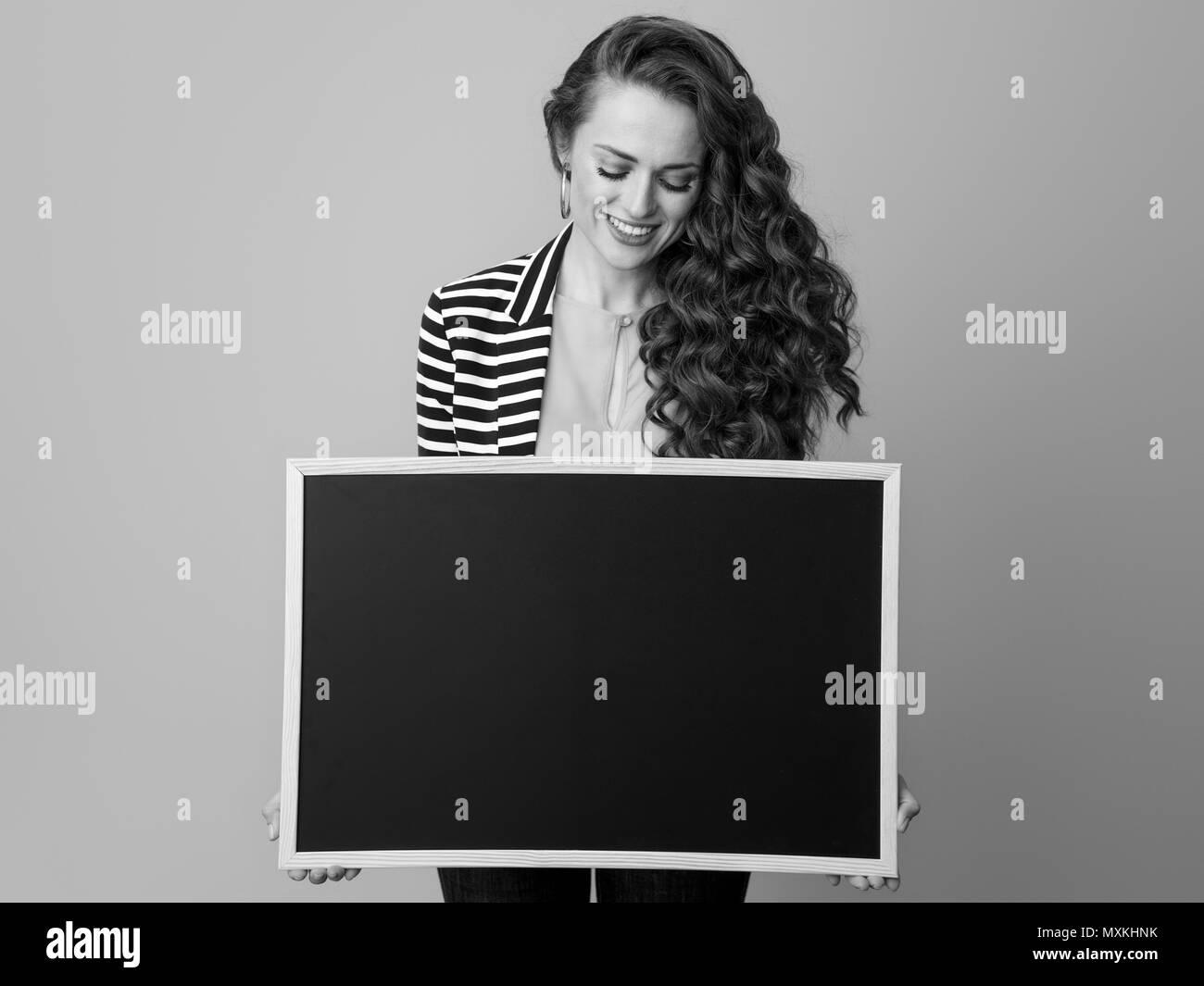 Gerne modernen Frau in gestreifte Jacke gegen Hintergrund auf Blank Board Stockfoto