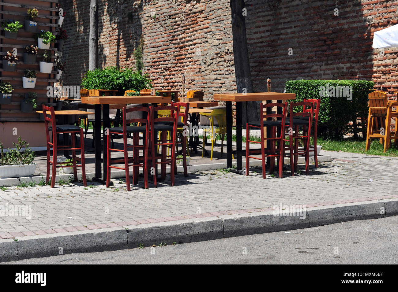 Leere Tische und Stühle in der albanischen Sidewalk Café. Blumenschmuck in Eimern an der Wand. Mauer im Hintergrund. Stockfoto