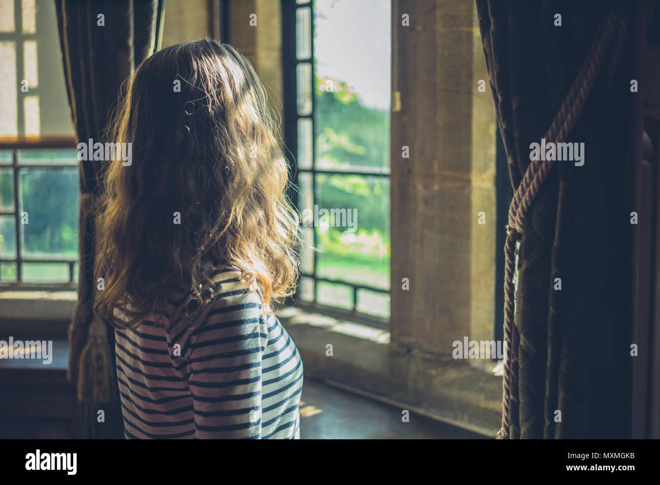 Eine junge Frau wird Blick aus dem Fenster eines Hauses in der Landschaft Stockfoto