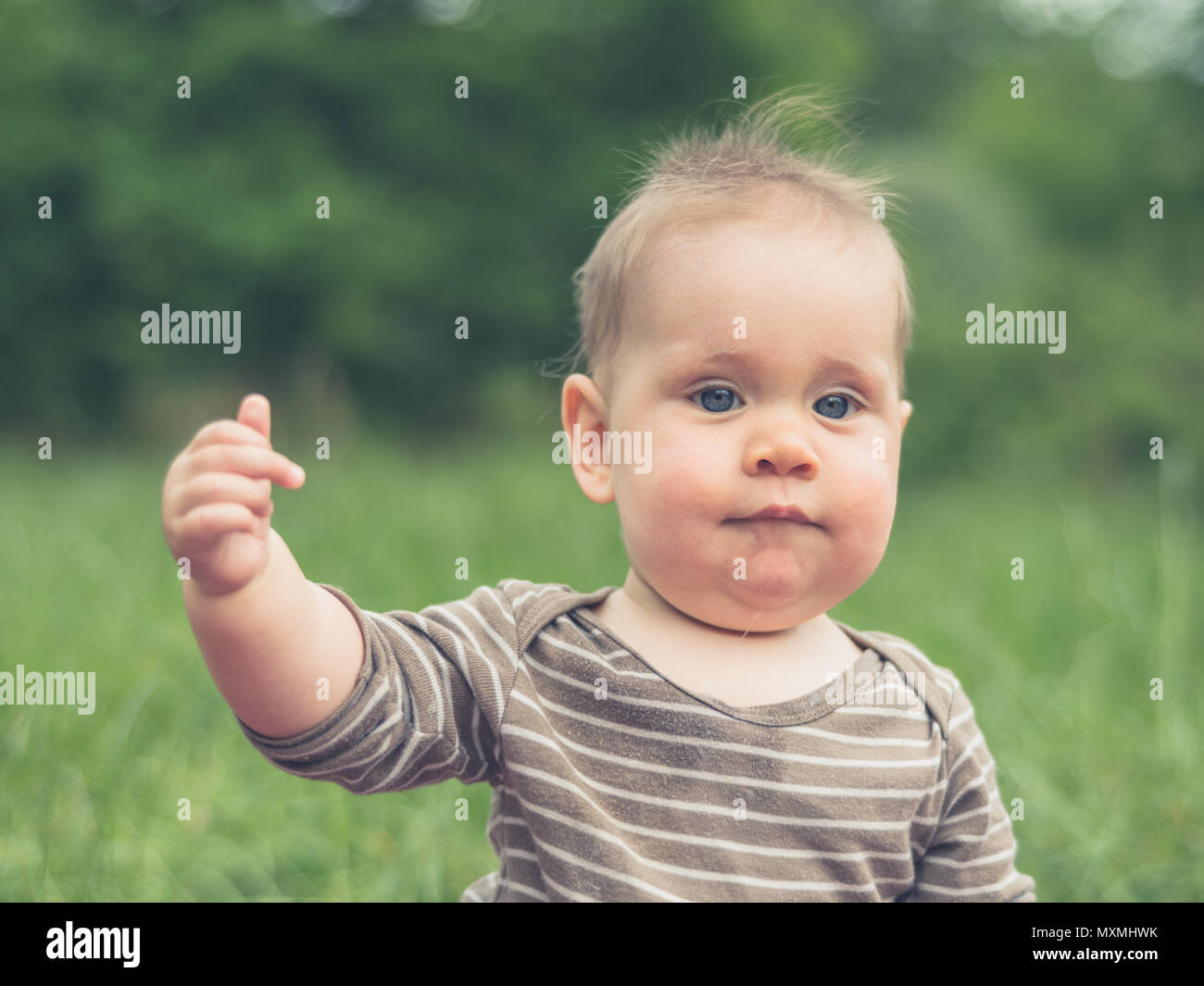 Ein süßes kleines Baby sitzt in der Natur und ist eine Geste mit seinem Mittelfinger Stockfoto