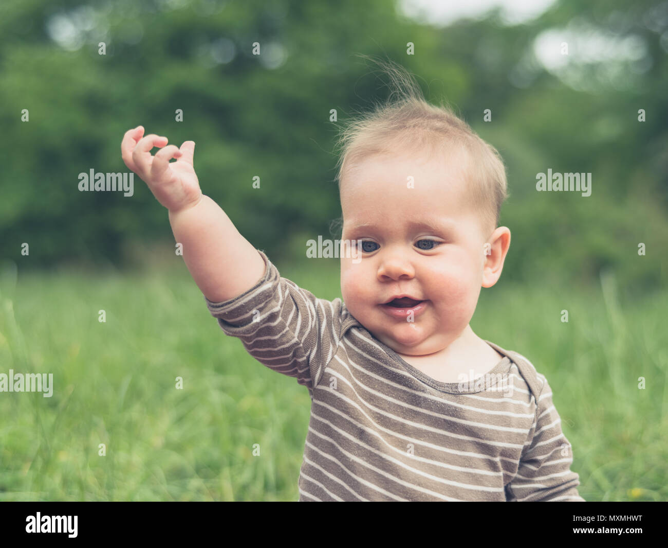 Ein süßes kleines Baby sitzt in der Natur und ist eine Geste mit seiner Hand Stockfoto