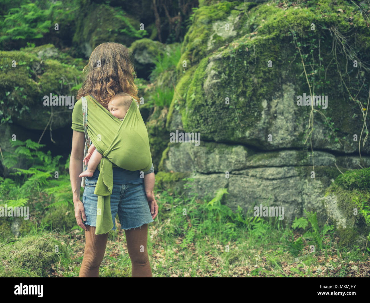 Eine ökologisch bewusste Mutter mit ihrem Baby im Tragetuch steht in der Natur Stockfoto