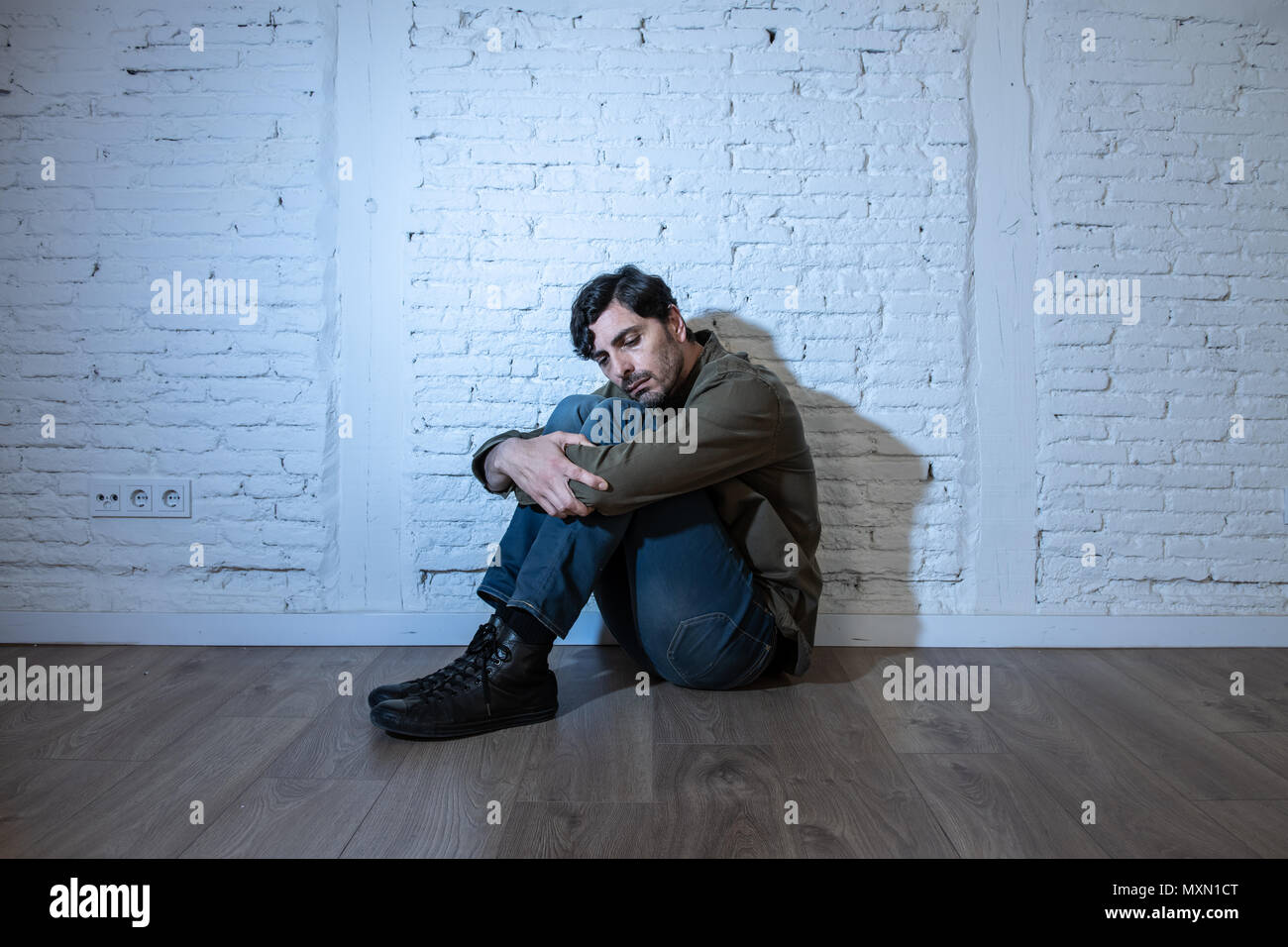 Junge depressiven Mann gegen eine weiße Wand zu Hause sitzen mit einem Schatten auf der Wand Gefühl miserabel, einsam und traurig in der psychischen Gesundheit Depression conce Stockfoto