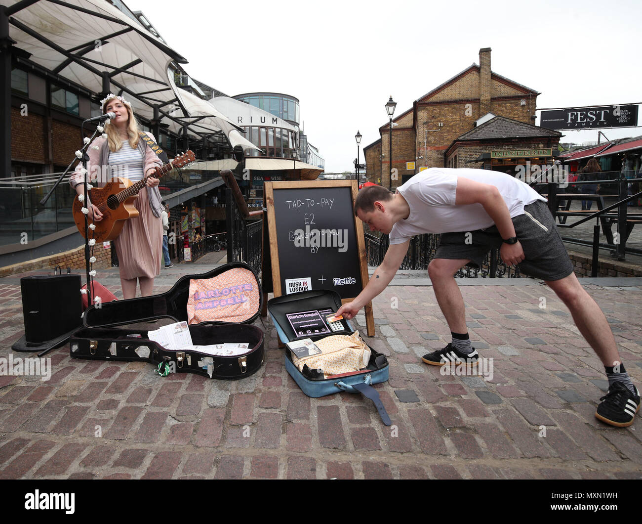 Busker Charlotte Campbell führt in Camden Market, nördlich von London, als Kate Jones, Programmdirektor bei Busk in London, schaut an. London hat erste kontaktlose Zahlung das Schema der Welt für Straßenmusikanten in Zusammenarbeit mit Technologieunternehmen iZettle gestartet. Stockfoto