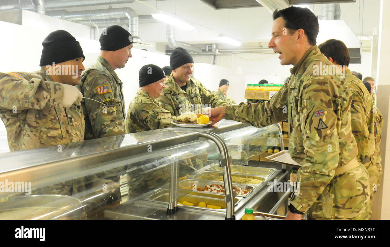 Ein Kaplan der US-Armee mit dem 2. Bataillon, 503. Infanterieregiment, 173. Luftlandebrigade, bietet einem britischen Soldaten während des Thanksgiving-Dinners am 25. November 2016 in Pabrade, Litauen, Bollard Greens an. Fallschirmjäger der Able Company, die an Übung Iron Sword 2016 teilnahmen, luden NATO-Verbündete ein, das Essen zu teilen. An der Übung beteiligen sich 11 NATO-Länder und 4.000 Soldaten, die die regionale Stabilität, die Partnerschaftsfähigkeit, das Vertrauen sowie die gemeinsame Ausbildung und Koordinierung der alliierten Streitkräfte fördern sollen. Stockfoto