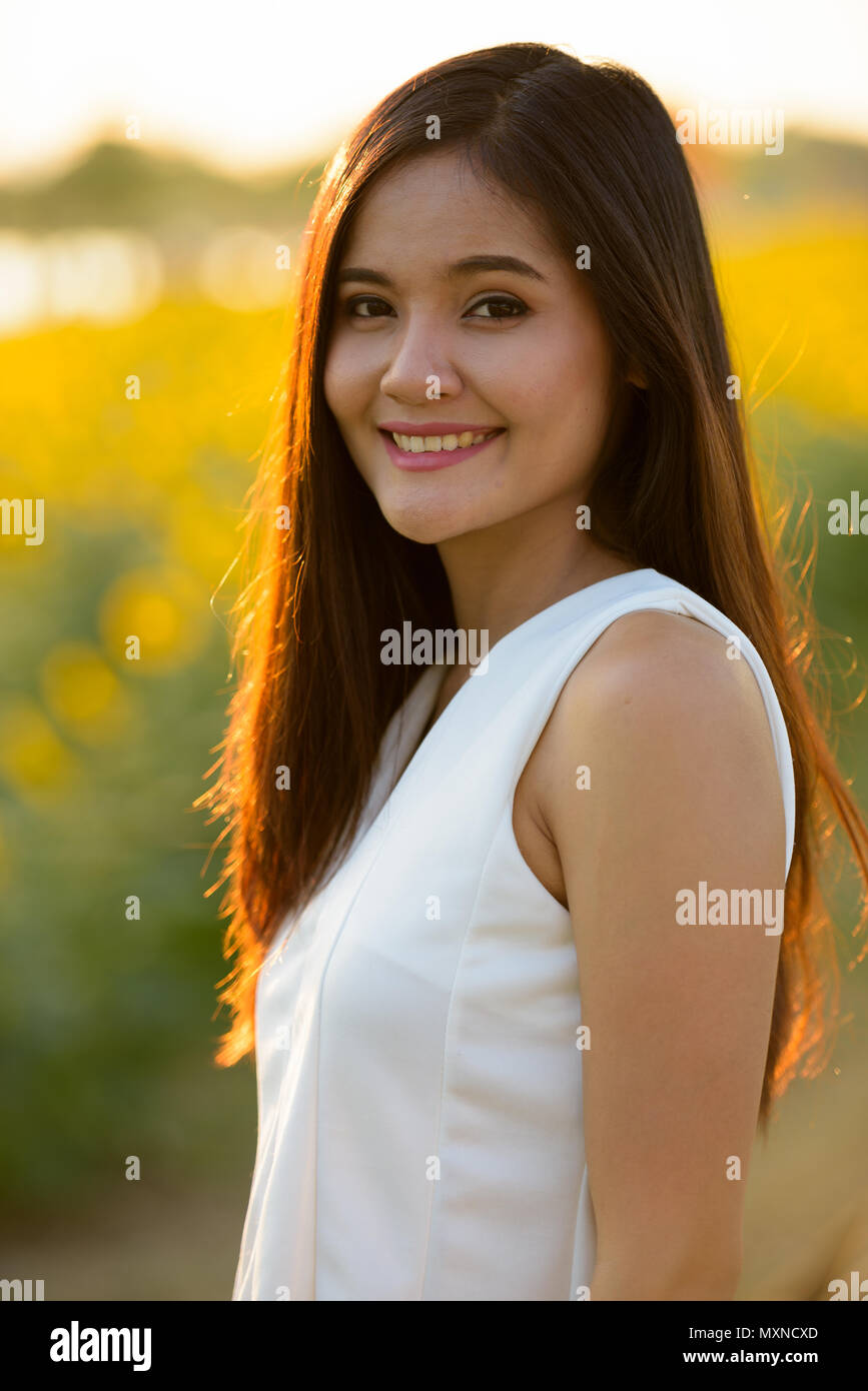 Junge asiatische Frau glücklich lächelnd gegen Feld der blühenden sunflo Stockfoto