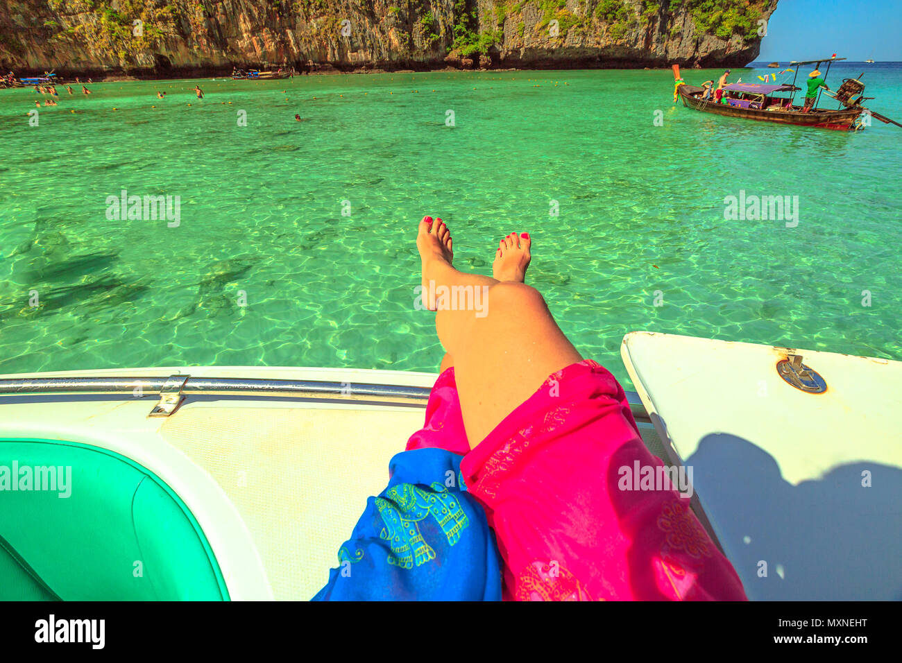 Frau gebräunte Beine auf einem touristenboot im tropischen und idyllischen Lagune des beliebten Maya Bay, Ko Phi Phi Leh in Phi Phi Island, Krabi, Andaman Meer. Urlaub, Lifestyle und Sonnenbaden Konzept. Stockfoto