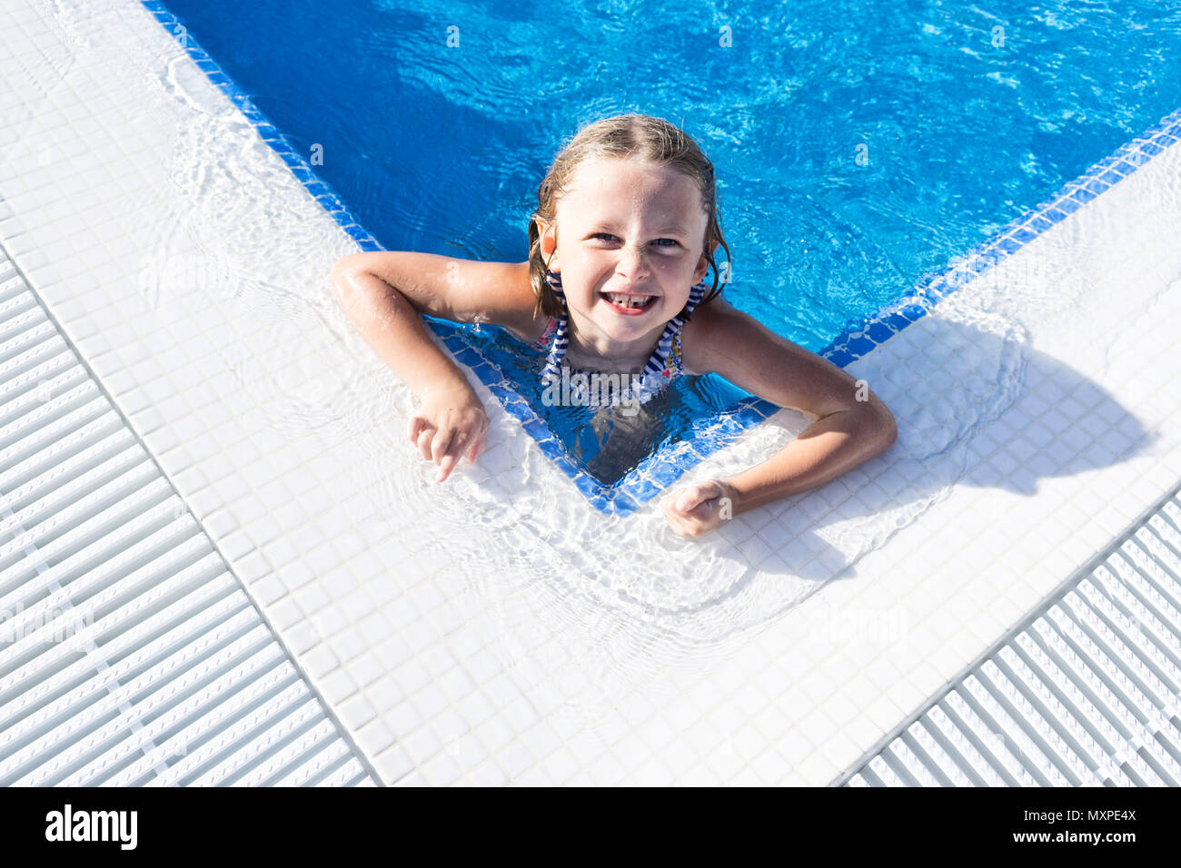 Weibliches Kind suchen, um sich von der Ecke aus einem Schwimmbad lächelnd Stockfoto