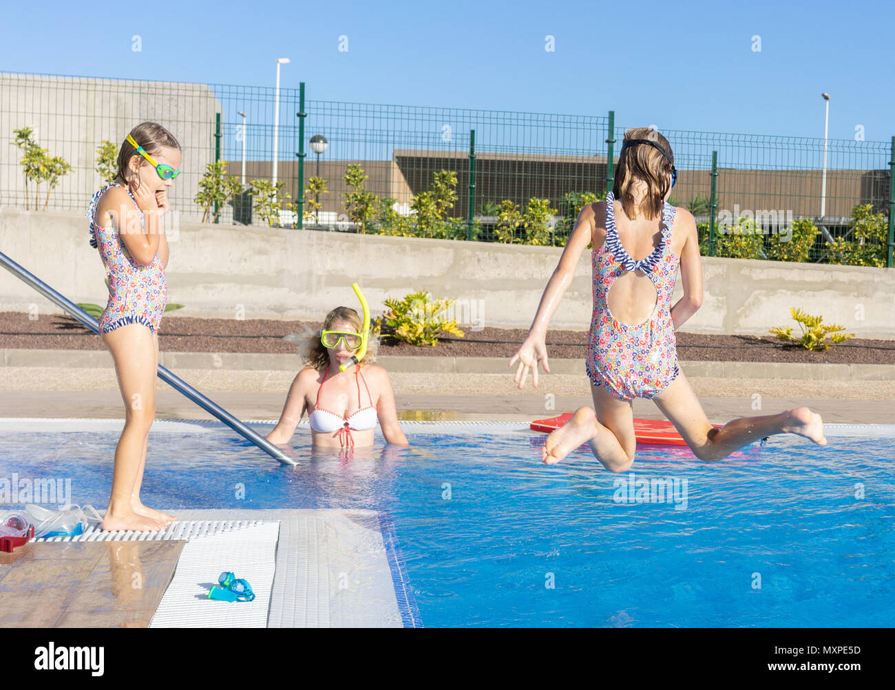 Weibliches kind Mitte Sprung in einen Pool mit ihrer Schwester und Mutter beobachten Stockfoto