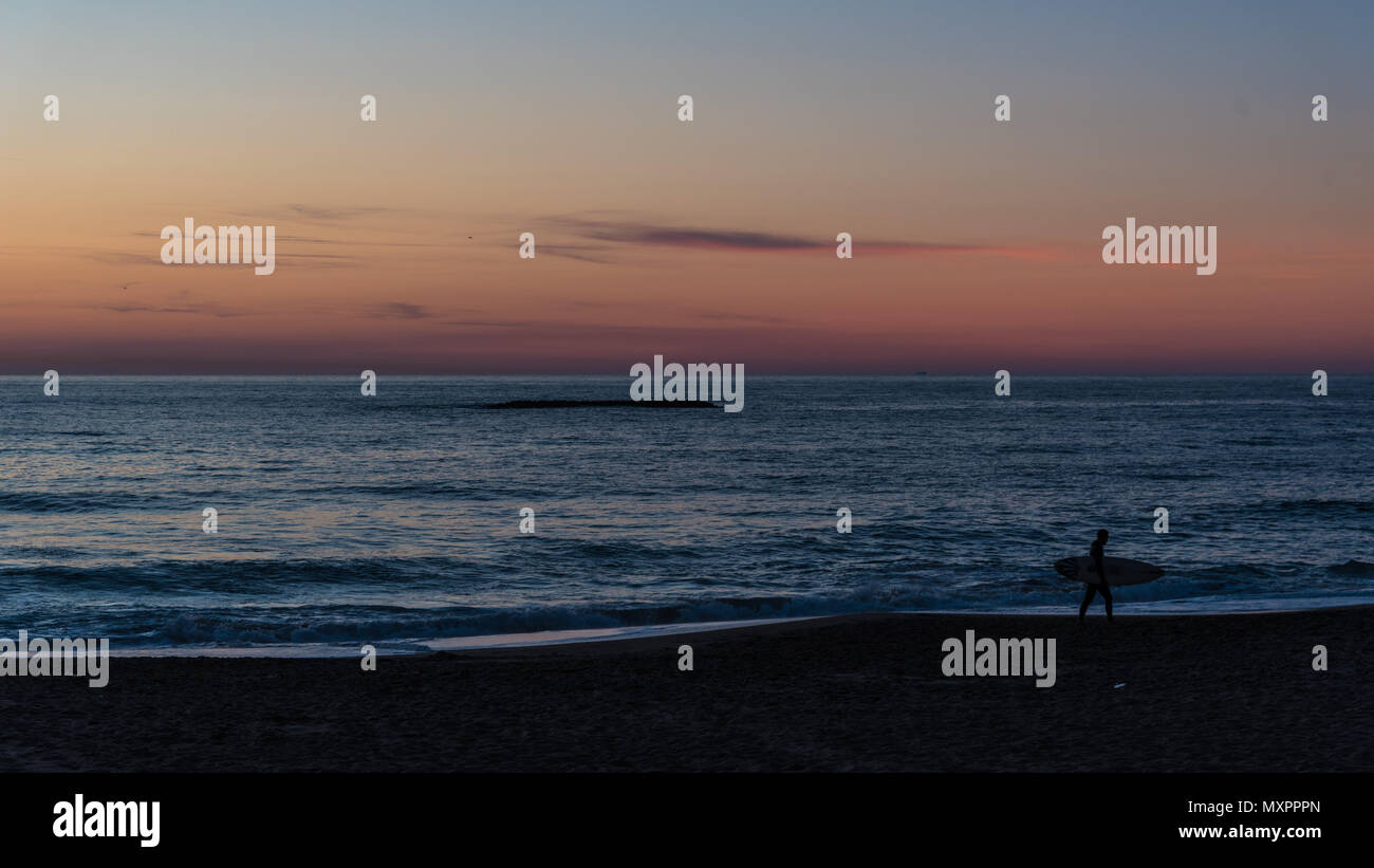Ein Surfer zu Fuß entlang der Strand bei Sonnenuntergang Stockfoto