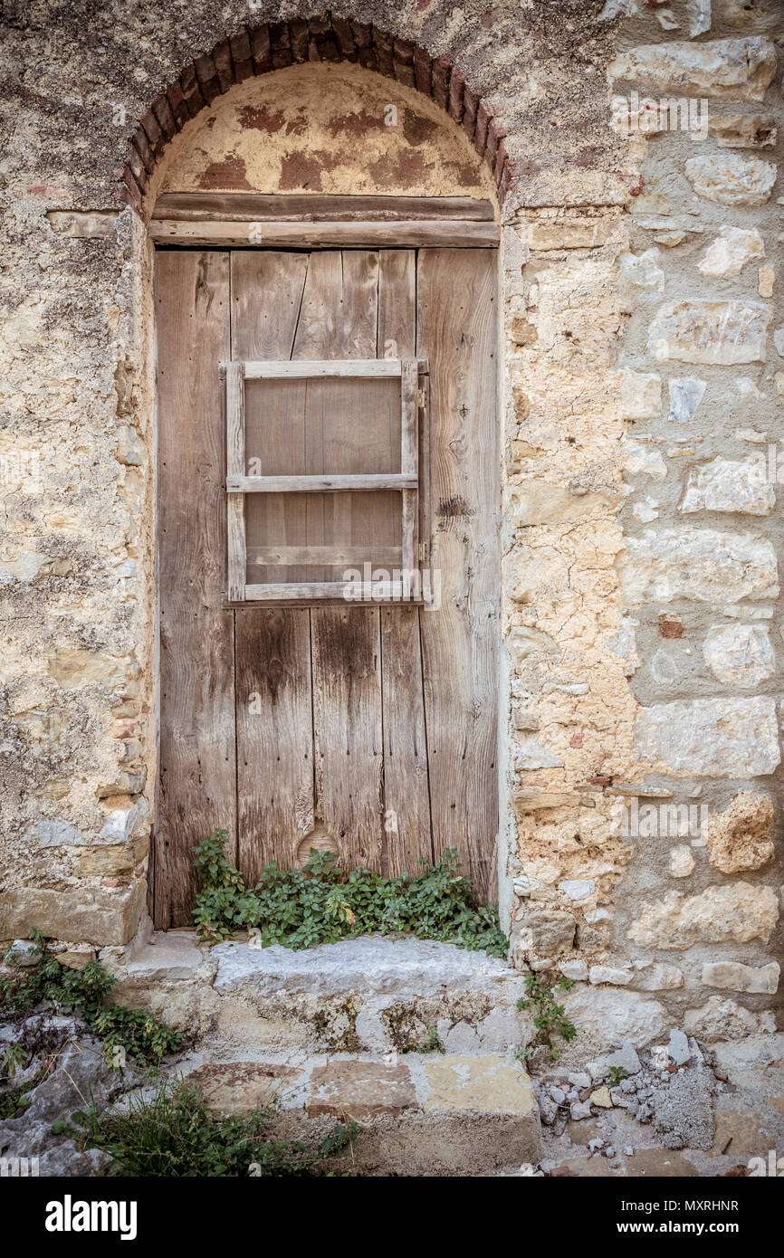 Alte braune Holztür und schmutzige Mauer aus Stein. Pflanzen, die in der vorderen Tür und zwei steinerne Stufen. Eingang zum Haus Stockfoto
