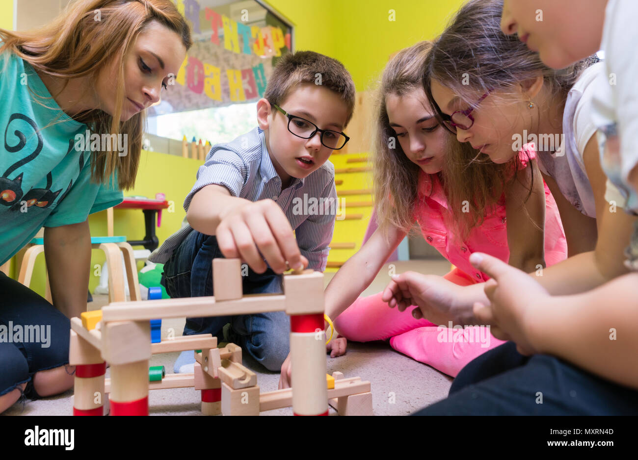 Engagierte Kindergärtnerin Kinder helfen mit dem Bau eines Zuges Stockfoto