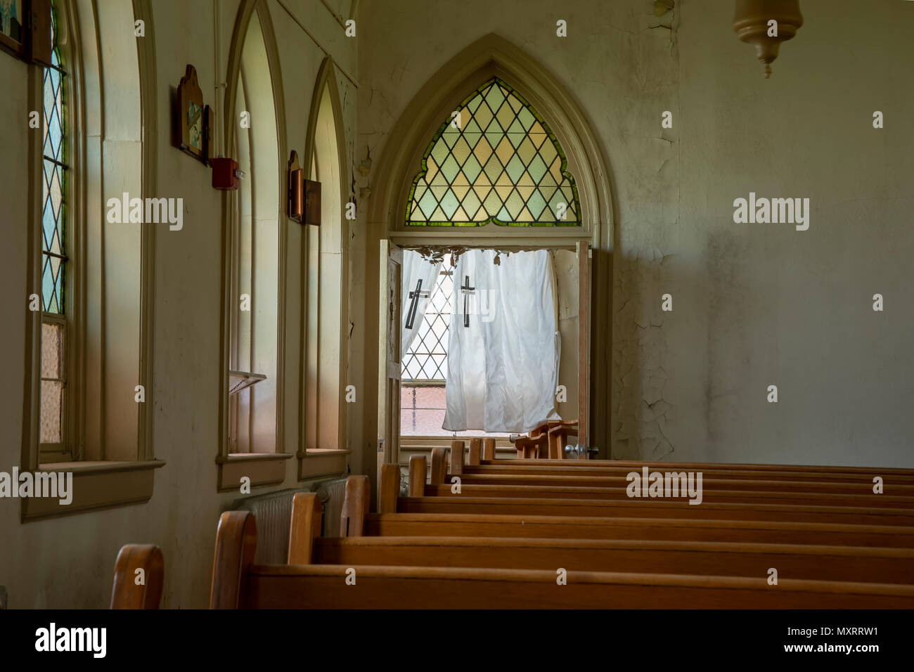 Innenraum der abgebrochenen Kirche mit Holzbänke mit Glasfenstern und Kreuze auf weißen Vorhängen. Stockfoto