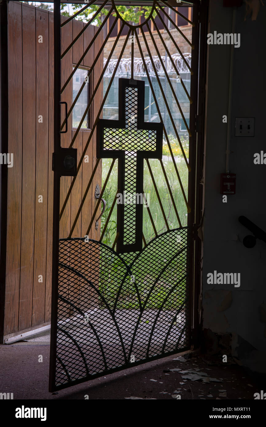 Licht durch Metal Gate kommen mit Kreuz aus dem Inneren der Kirche in den Gefängnishof mit Stacheldraht. Stockfoto