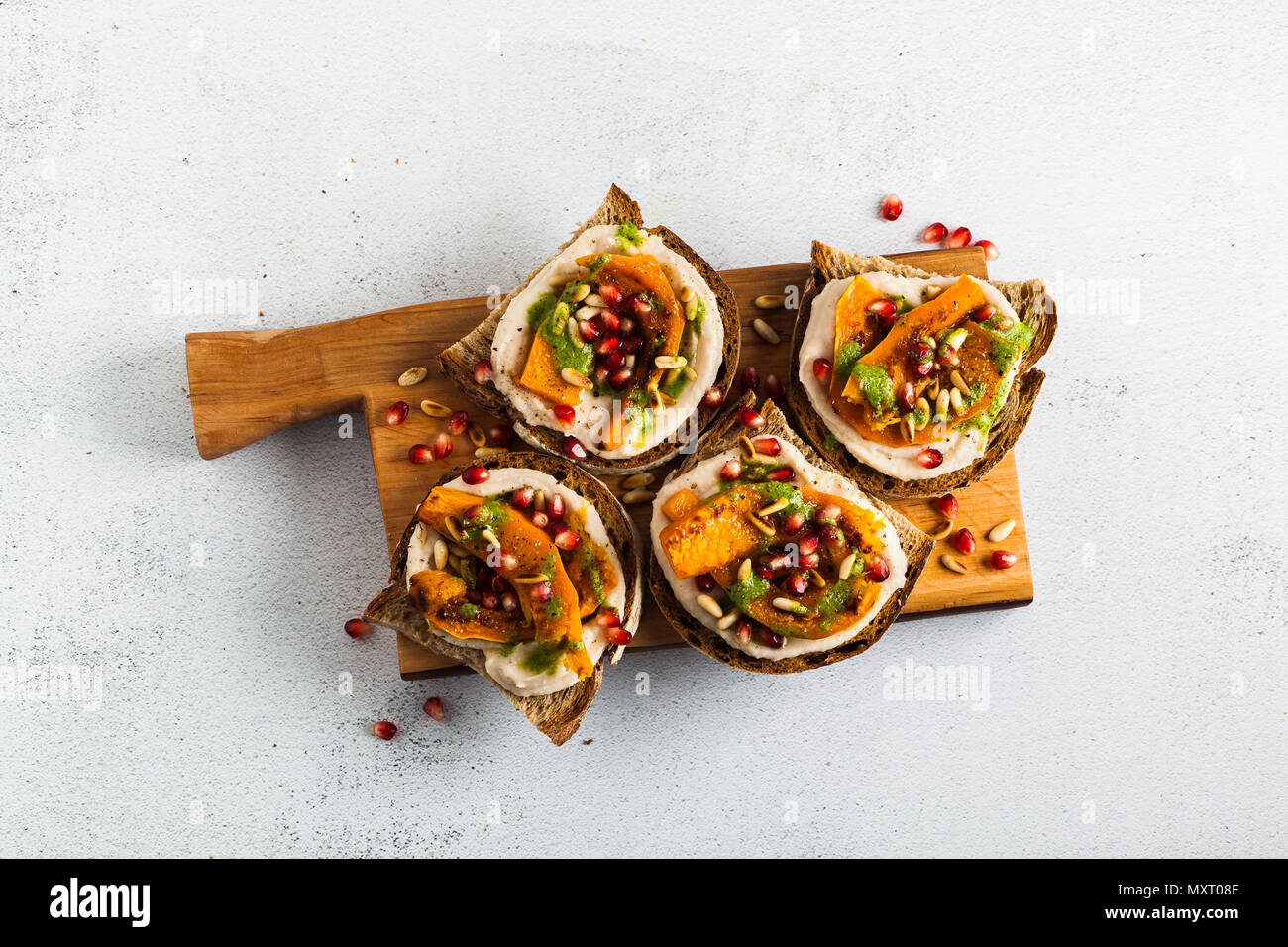 Snack Brote mit Hummus und gebackenen Kürbis auf einer Platine mit Rucola Pesto. Samen von Granatapfel und Pinienkernen. Gesundes Essen Stockfoto