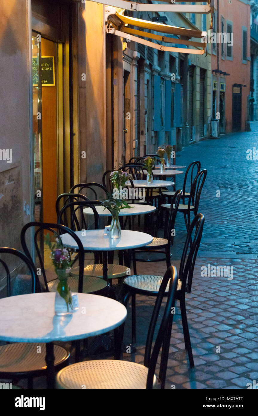 Kleine Kopfsteinpflasterstraße in Rom mit Tischen und Stühlen am Abend Stockfoto