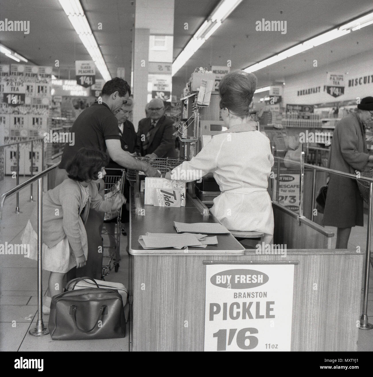 1960, historische, Vater mit jungen Tochter zu helfen, mit ihren eigenen Einkaufstaschen an der Kasse auf eine neue Art von Retail Store, ein SB-Shop, einen sogenannten "Supermarkt", England, UK. Es war nach dem Ende der Rationierung im Jahre 1954 beim Personal Konsum begann zu wachsen und in den 60er Supermärkte, so wie wir sie heute kennen, begann eigentlich in Großbritannien zu entwickeln, obwohl viele der ursprünglichen Marken mit anderen Ketten zusammengeführt oder berücksichtigt wurden. Stockfoto