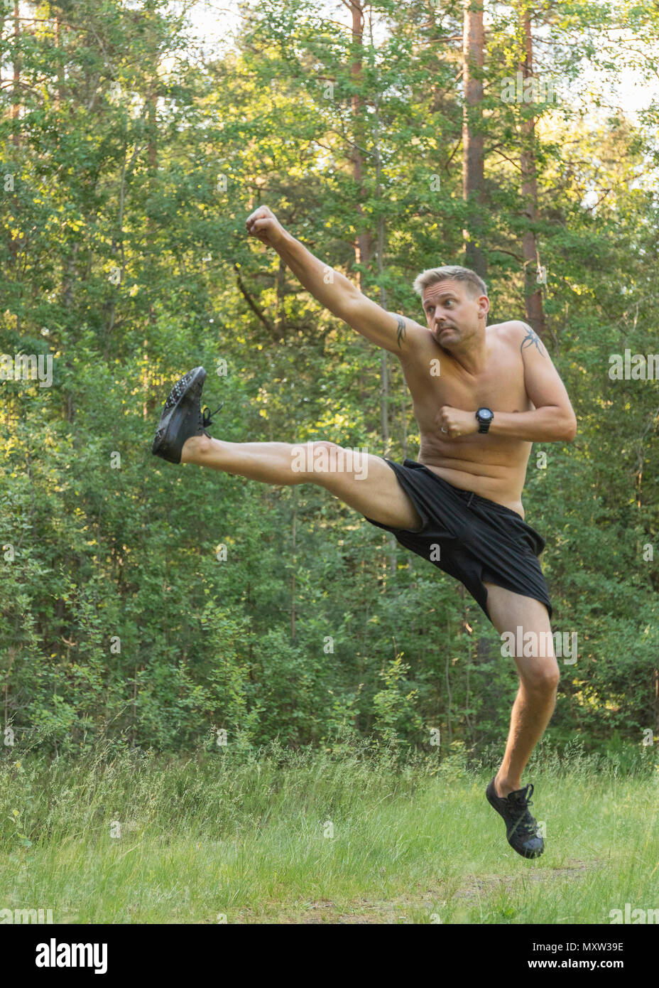 Mitte nach 40 s kaukasischen Mann barechested springen, Schlagen und Treten praktizieren Kampfkunst draußen im Wald Stockfoto