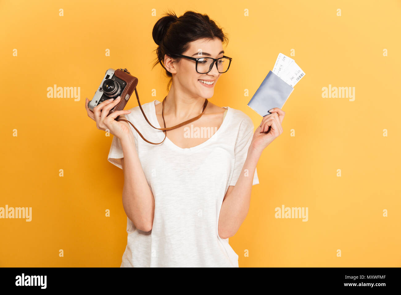 Das Bild der jungen Frau touristische Fotograf Brille auf gelben Hintergrund holding Passport mit Tickets und Kamera isoliert. Suchen asid Stockfoto