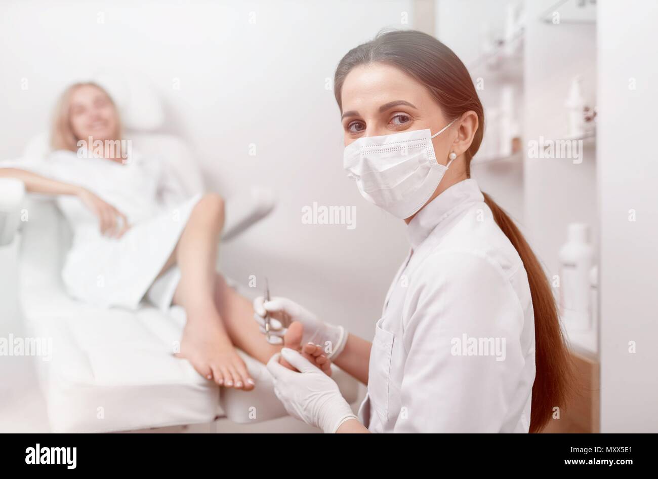 Fußarzt in der Maske auf das Gesicht auf Kamera und Arbeiten. Stockfoto
