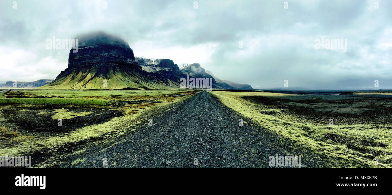 Einsame schwarze Straße durch das grüne Gras und der vulkanischen Landschaft im Süden von Island Stockfoto