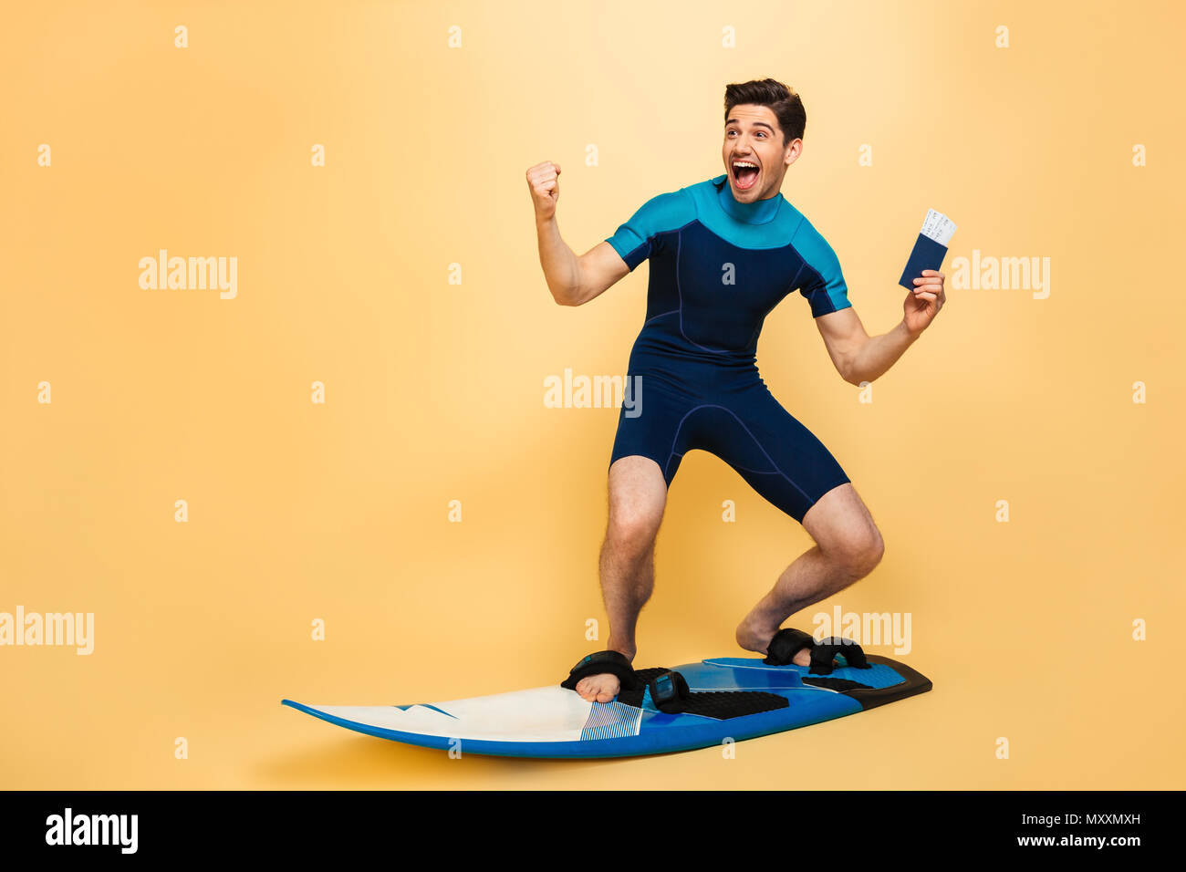 Foto von einem emotionalen junger Mann im Badeanzug auf gelbem Hintergrund auf Surfen board Holding Tickets und Reisepass isoliert gekleidet. Stockfoto